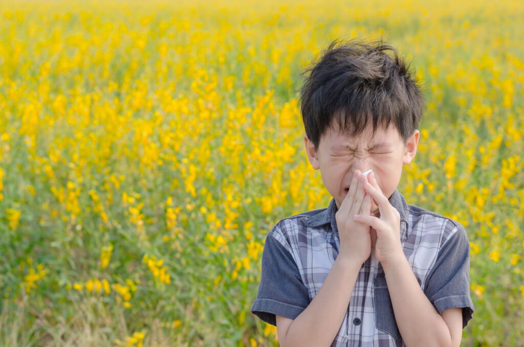 Boy blowing his nose in a field of flowers.
